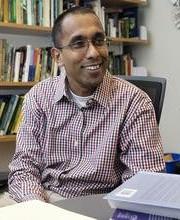 Dr. Thilina Surasinghe sitting at his office desk with bookshelves in background