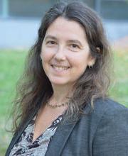 Brenda Kozuch smiling with dark brown wavy long hair wearing a charcoal gray blazer over a v-neck gray and black top