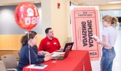 Darren Smith sits at a table and talks to a fellow student who is standing in front of table 