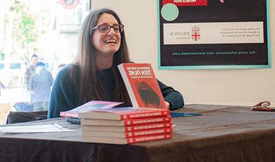 Michele Meek sits at a table with copies of her book on display