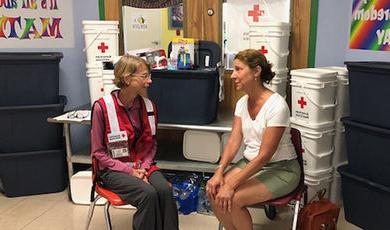 Maggie Lowe, wearing a Red Cross vest, talks with a flood victim.