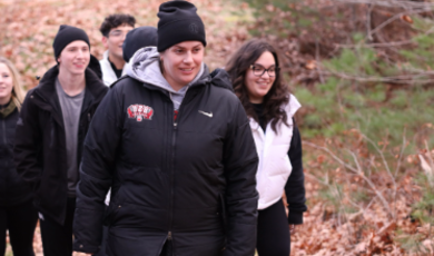 Woman wearing black hat and jacket leads a group of people on path in the woods 