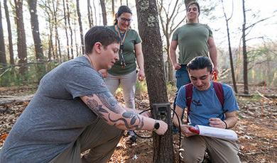 Students and a professor attach a camera to a tree in the woods.