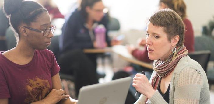 Professor speaking to a student at the student's desk and computer