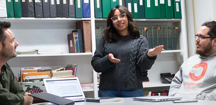 A student giving a presentation in Spanish while Professor 瑞安LaBrozzi and another student look on