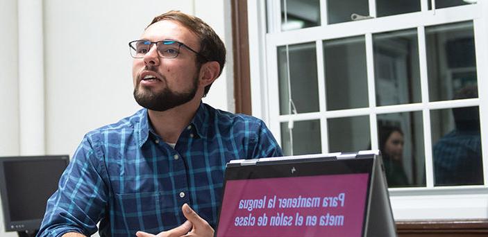 A student gives a presentation in Spanish next to his open laptop that shows the title of the presentation in Spanish